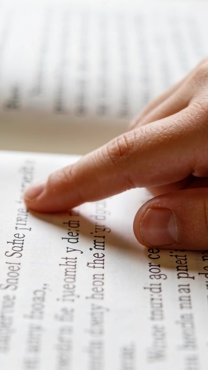 Vertical video: Tracing right index finger moving along printed line on open book, tracking words
