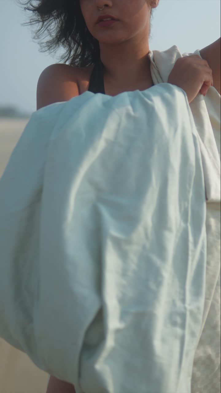 Vertical Close-Up Tight shot of woman’s arms holding light fabric on sandy beach