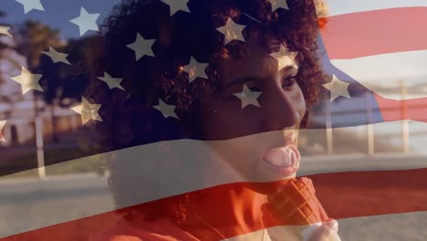 animation of flag of america waving over african american young woman with afro hair eating icecream