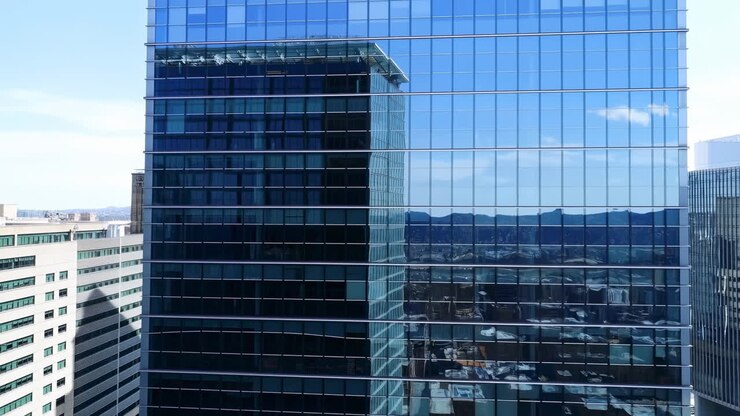 Rascacielos de cristal reflejando el horizonte de montañas azules, exterior panorámico de sede corporativa con fachada de espejo.