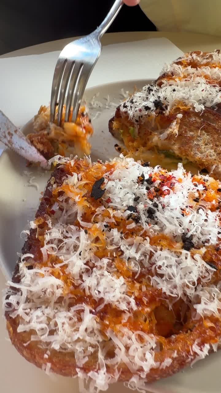 Mano che taglia un delizioso toast al formaggio con formaggio grattugiato.