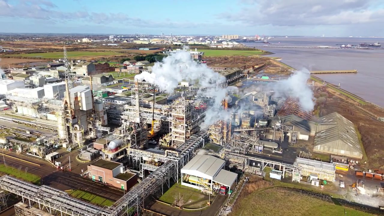 Aerial view of a sprawling industrial chemical manufacturing plant with thick smoke billowing from a chimney stack in Grimsby, Lincolnshire, UK.