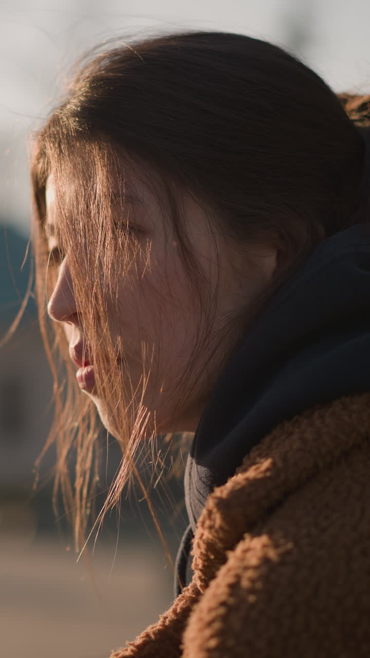 Close-up of a girl wearing a brown coat, with her hair partially covering her face. She appears sad and lost in thought, her expression reflecting a profound sense of sadness and emotional turmoil