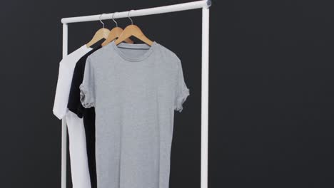 video of three white, black and grey t shirts on hangers and copy space on black background