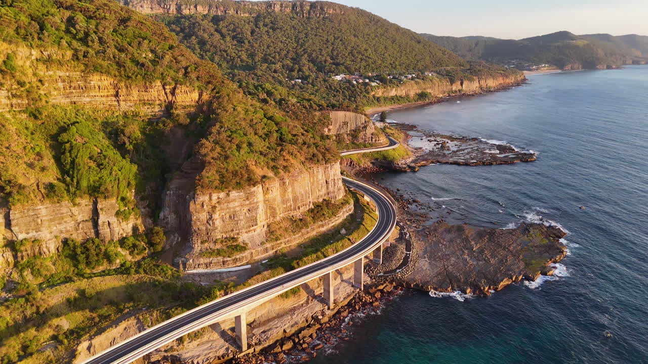 Aerial footage of the Sea Cliff Bridge, rising drone shot of the curving road above the blue waters of the Pacific.