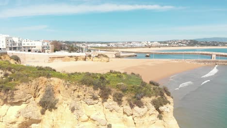 Batata-Beach-barred-by-Eroded-cliffs-and-Solaria-pier-in-Lagos,-Algarve,-Portugal---Aerial-Slide-tracking-shot