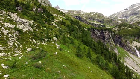 un ripido pendio coperto di erba con un sacco di pietre accanto a un'enorme scogliera e una grande cascata nelle alpi a kaernten, in austria