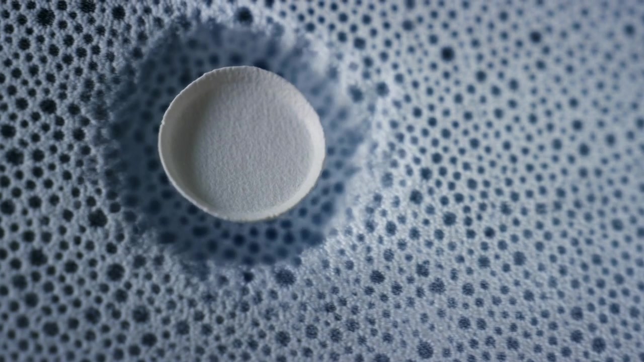 Tight overhead macro view of single round effervescent tablet seated at center of dense microbubble foam within circular container