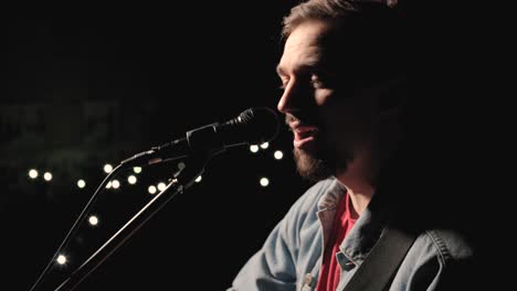 a musician is playing guitar on a large stage with audience members holding flashlights in the background. the auditorium is filled with beautiful flashing lights.