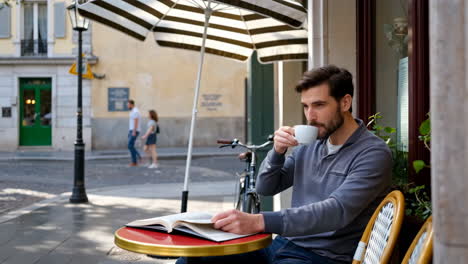 man reading a book and drinking coffee at an outdoor cafe