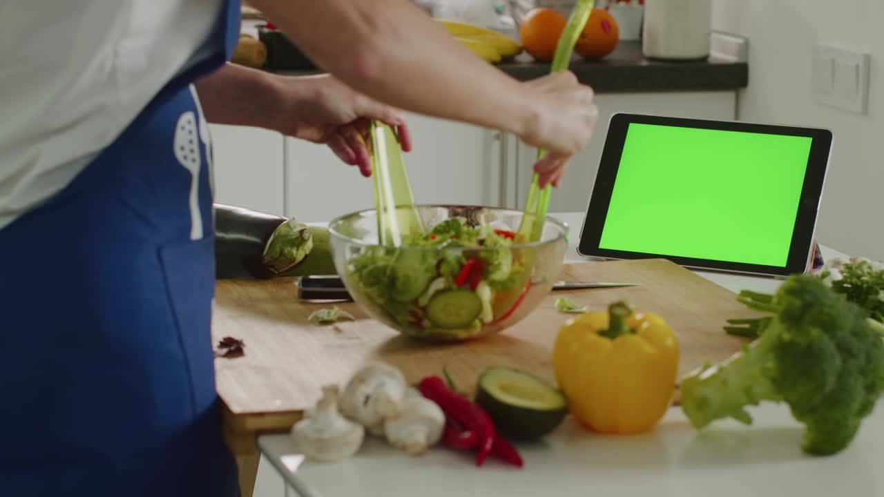 la mujer está mezclando la ensalada y mirando la tableta. tableta con una pantalla verde. preparación de ensalada. 4k