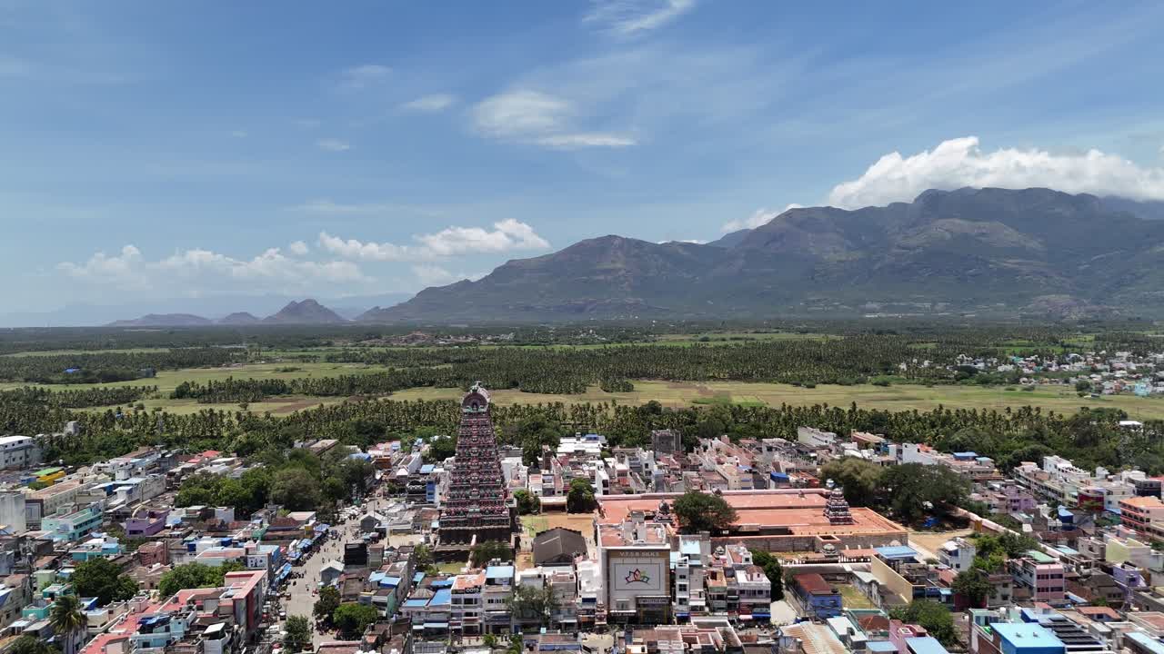 Beautiful aerial shot of Tenkasi Temple in Tamil Nadu with the Western Ghats behind, showing the ancient gopuram, green fields, and colorful town under clear blue skies