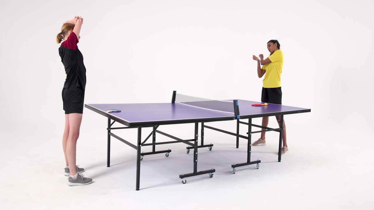 Stretching before playing table tennis, two women standing by table tennis table