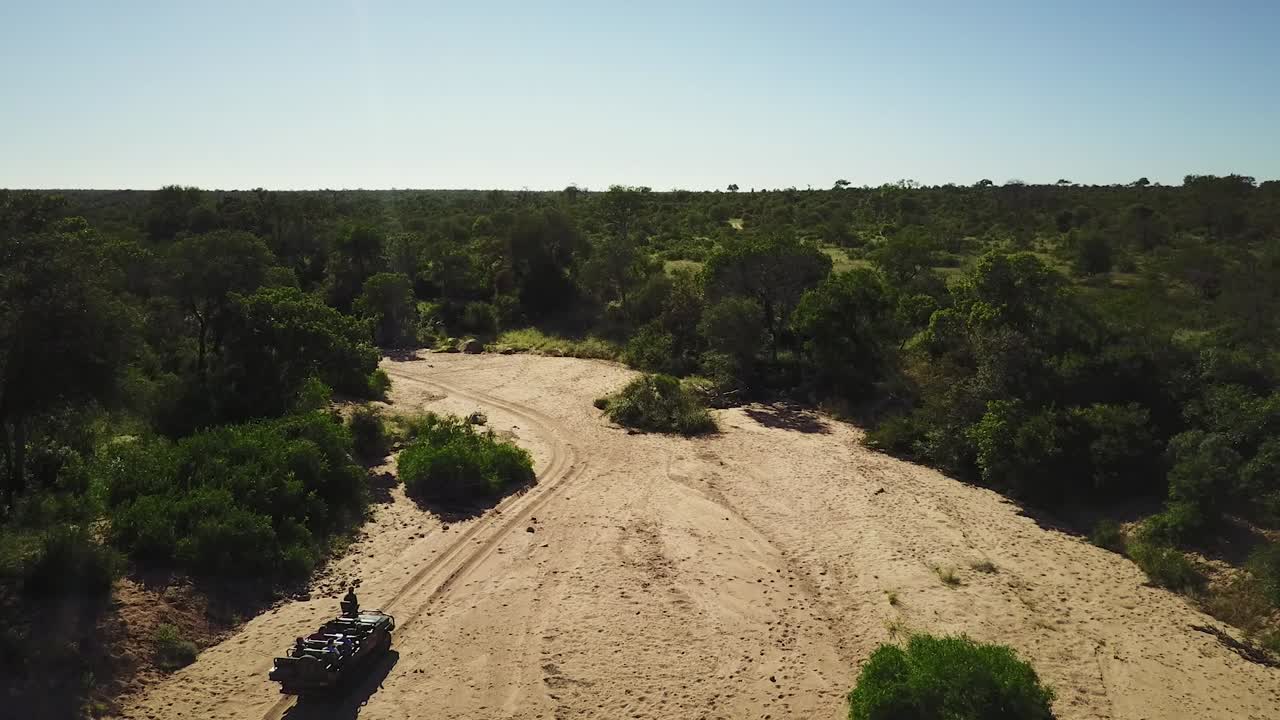 una toma de un drone de un vehículo de safari conduciendo a través de un lecho de río seco en áfrica