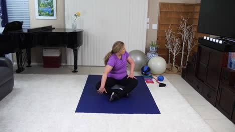 older woman performing twisting stretches cool down in home gym, static, locked off