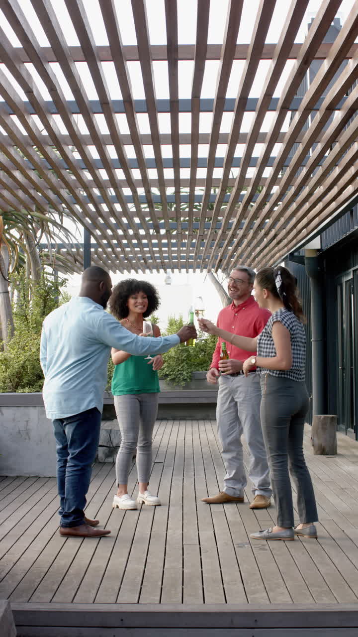 Vertical video of team of diverse happy colleagues toasting drinks together at office