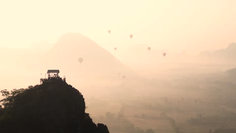 Toma-De-Un-Dron-Desde-Un-Mirador-Observando-Globos-Aerostáticos-Al-Amanecer-En-Vang-Vieng,-La-Capital-De-Aventuras-De-Laos.