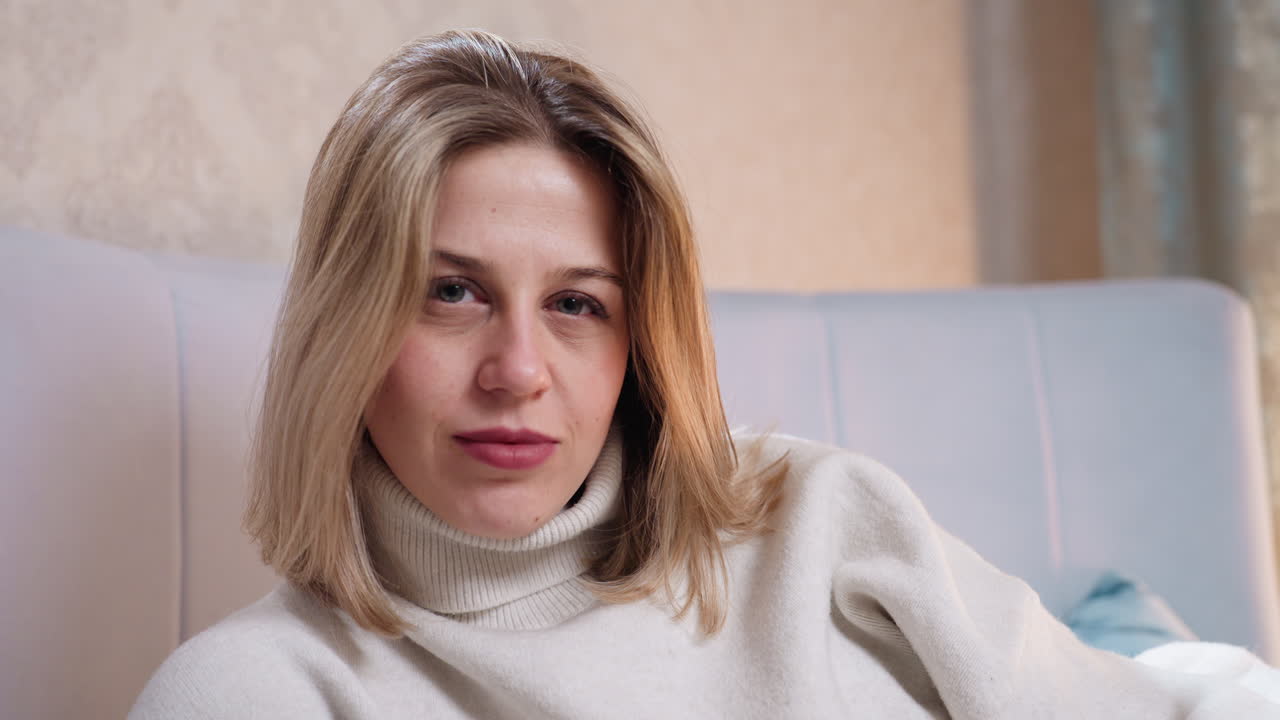 Woman wearing light sweater sitting on bed looking directly into camera with calm expression, creating intimate portrait full of confidence, warmth, authenticity, natural beauty indoor lifestyle