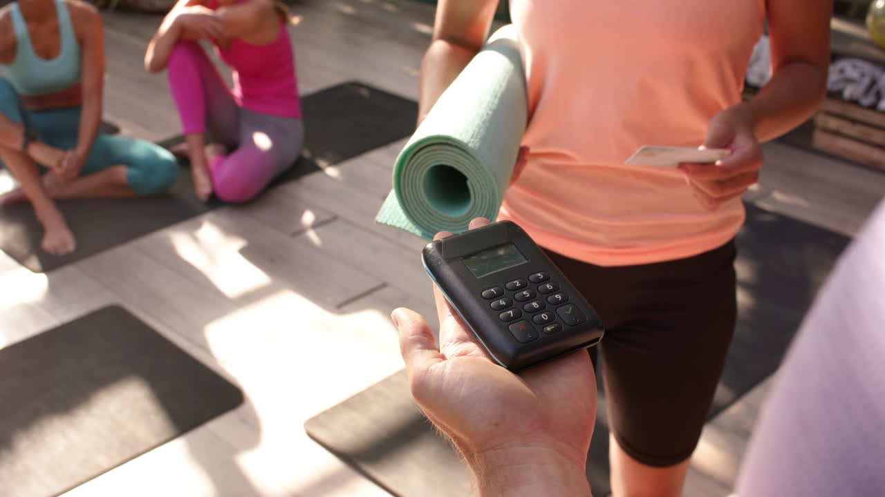 Paying for yoga class, woman holding yoga mat and credit card in studio