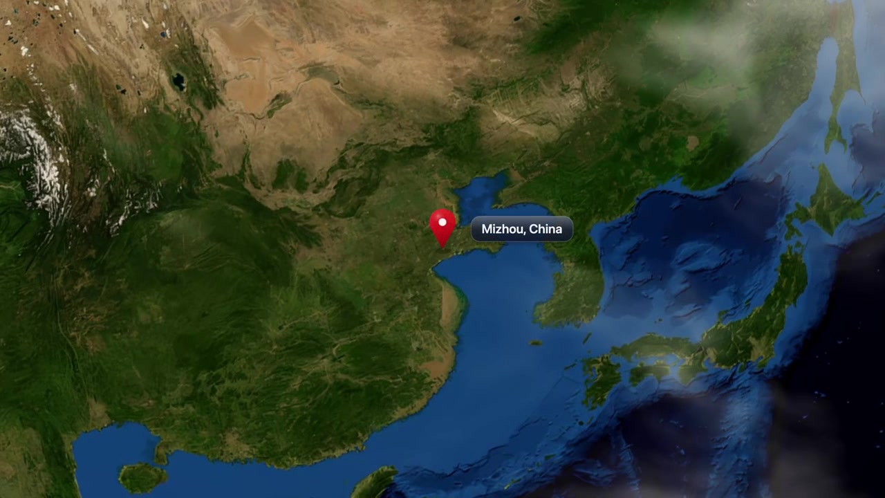 Satellite animation zooms from deep space into Mizhou, China, marking the location with a pin. Includes NASA public domain imagery.