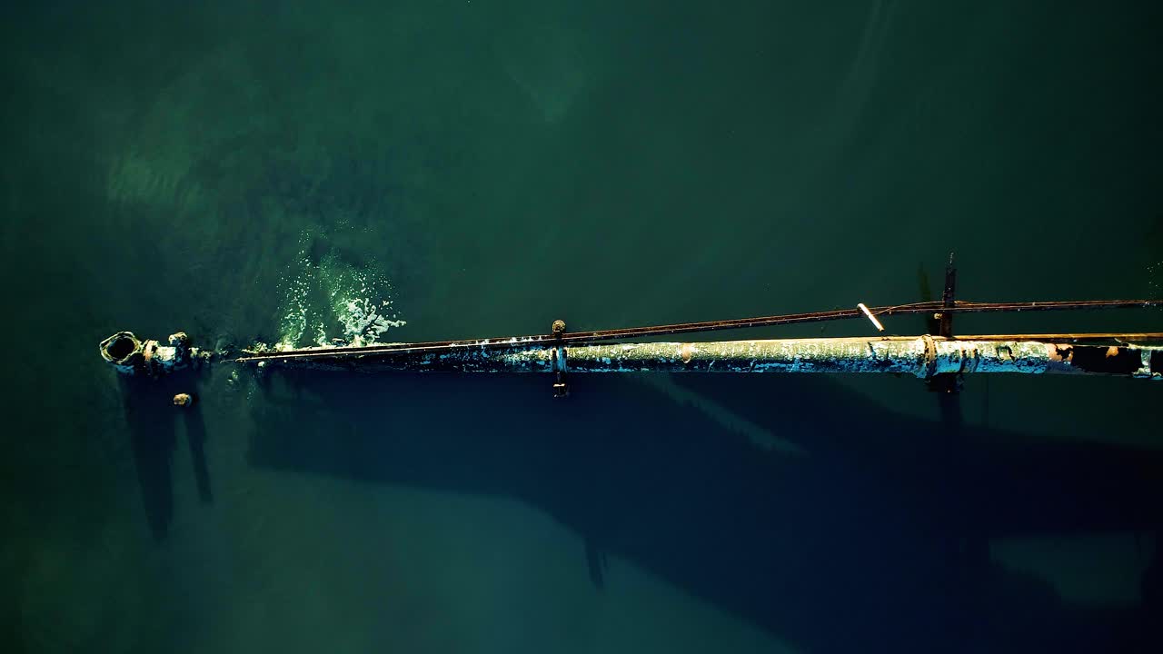 녹슨 새는 파이프가 맹그로브 숲으로 둘러싸인 호수로 흘러 들어가 하수를 버리는 낮은 공중 하향식 샷