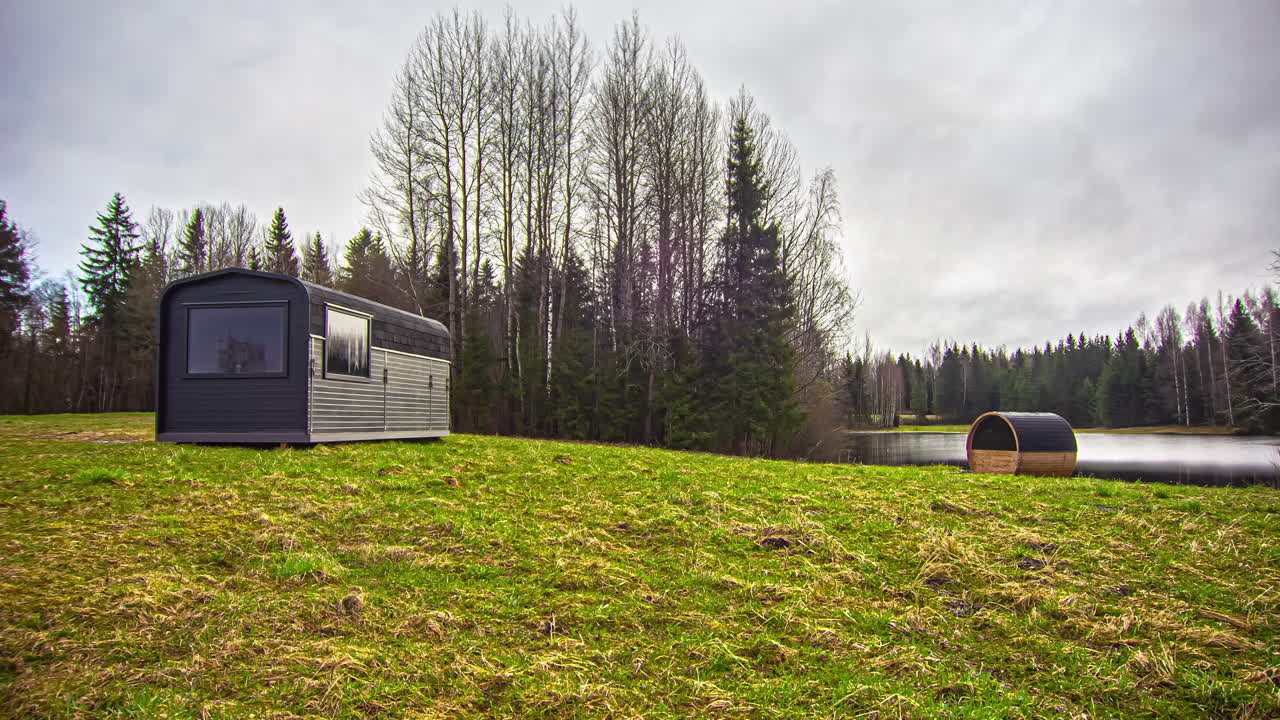 해가 뜰 때부터 해가 질 때까지 무성한 녹색 외딴 지역으로 둘러싸인 배럴 사우나가 있는 나무 오두막의 멋진 샷