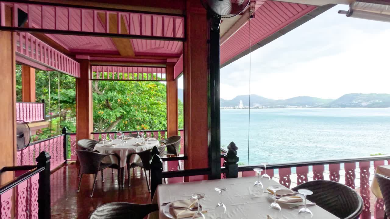 Elegant dining tables on a covered balcony with ocean view, natural daylight, gentle camera pan