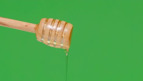 4k. fresh honey pouring and flowing from wooden dipper spoon on green background