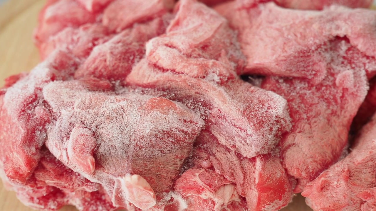 氷の結晶で覆われた冷凍生肉の塊のクローズアップ。