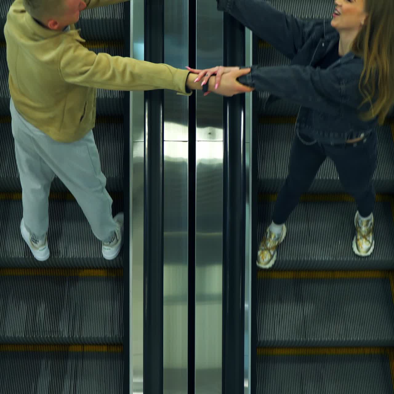 Modern escalator stairs moving quickly in the mall. Woman and man going by opposite lines stretch their hands to each other. Top view