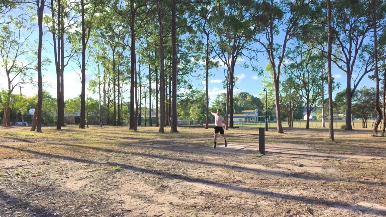 Hombre caucásico lanzando un disco jugando disc golf en un parque público en un día soleado en Logan, Brisbane, Queensland, Australia