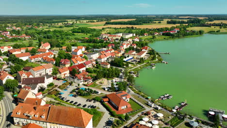 Aerial-view-of-Ryn,-Warmia-Masuria,-with-its-lakeside-marina,-colorful-buildings,-and-surrounding-fields