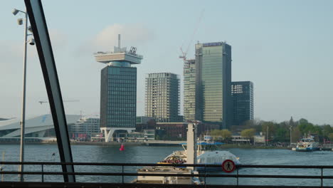 Ferry-En-El-Río-Amstel-Amsterdam,-Vista-Desde-La-Plataforma-Del-Autobús-De-La-Estación-Central,-Tiro-Panorámico-Con-Gaviotas-Voladoras