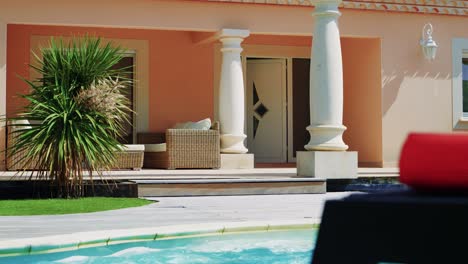 white door of a villa that opens alone, columns, small palm tree and swimming pool in the foreground