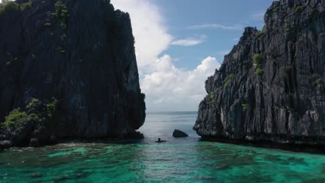drone aéreo volando a través de enormes acantilados de piedra caliza, agua turquesa y archipiélago natural con rocas y pequeñas embarcaciones en el nido, palawan, filipinas