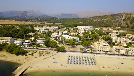 Panorámica-Con-Drones-De-Derecha-A-Izquierda-Del-Cuadro-Que-Muestra-La-Extensión-De-La-Playa-Del-Port-De-Pollença,-Un-Destino-Turístico-En-Mallorca,-España.