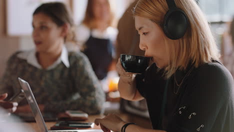 joven asiática que usa una computadora portátil trabajando en una cafetería escribiendo correos electrónicos compartiendo mensajes en las redes sociales usando auriculares disfrutando de escuchar música en un restaurante ocupado bebiendo café