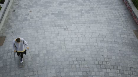 top view of the man with one leg on crutches riding his skateboard on circles.