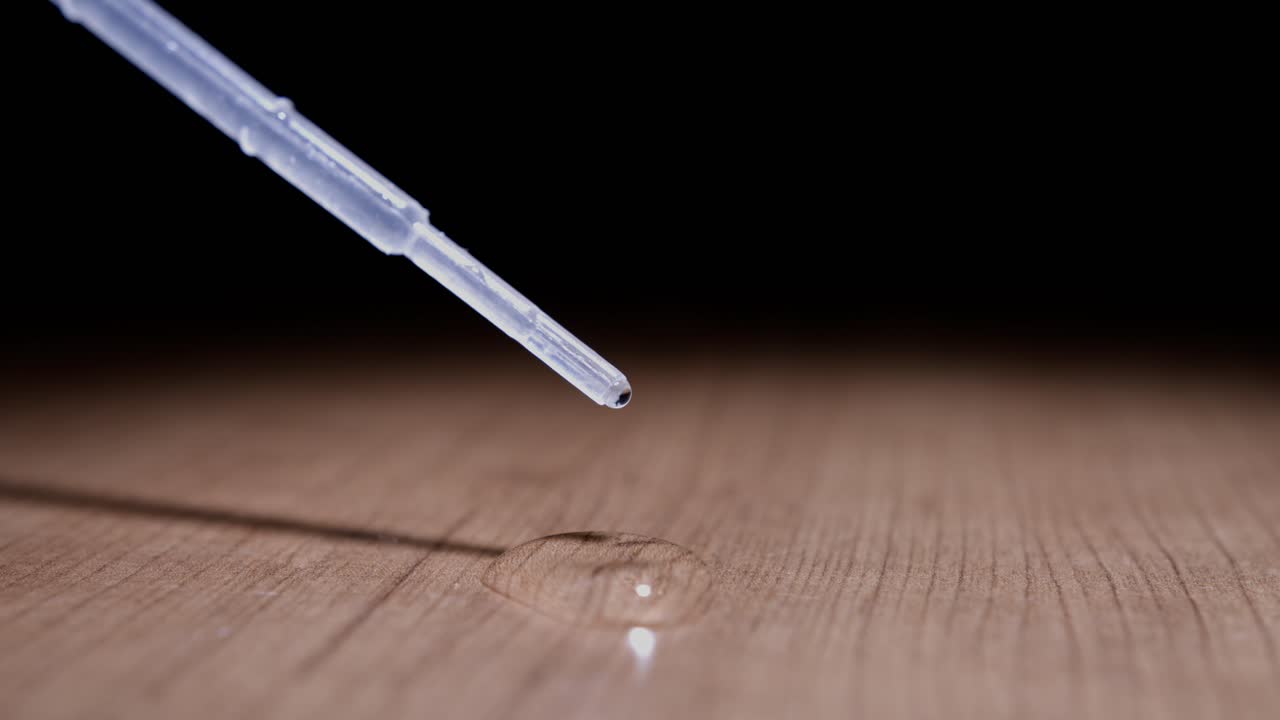Water drop falling from pipette creating a small water droplet on wooden surface