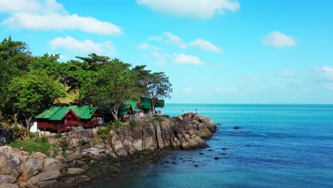 beach cabins over rocky coastline of tropical island with green vegetation, blue turquoise lagoon reflecting bright sky with white clouds in vietnam