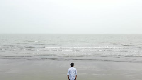 single lonely man standing at grey beach bad weather, getting startled