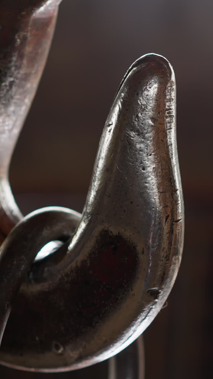 Old metal hook with hanging load on blurred background in warehouse closeup. Steel connecting part of lifting machine in industrial plant workshop