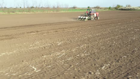 aerial circling view of tractor as dragging a sowing machine over agricultural field, farmland