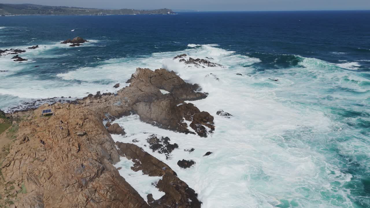Aerial view of turquoise waves crashing on rocks on the chilean coast at playa chica near valparaiso. rising shot