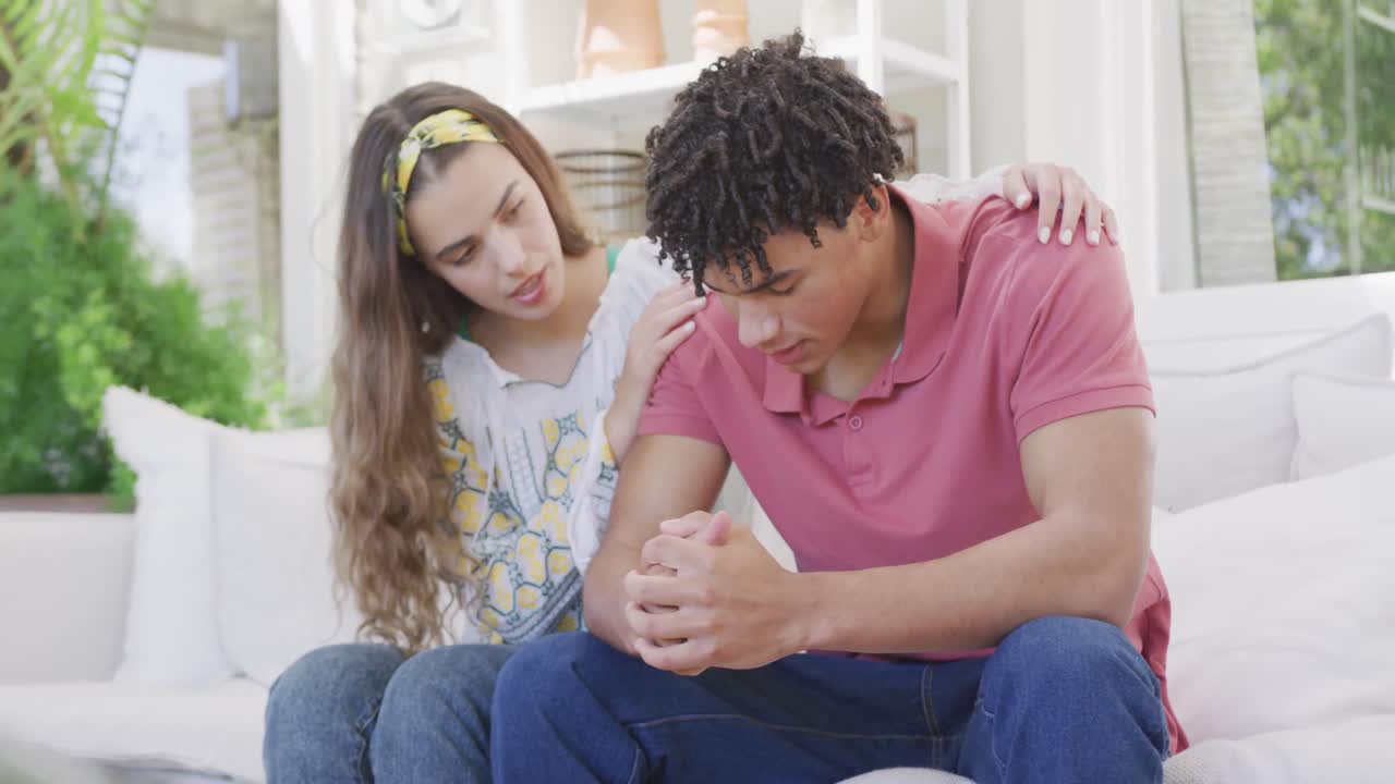 슬픈 이중 인종 부부가 집에서 함께 소파에 앉아서 환호하고 있습니다.