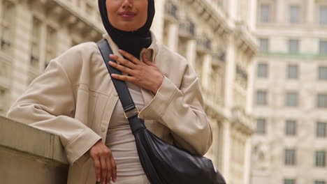 portrait of smiling muslim businesswoman wearing hijab and modern business suit standing outside city office buildings 9