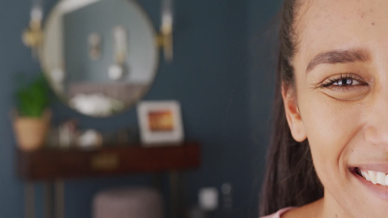 Video portrait of half the face of biracial woman smiling in bedroom at home, with copy space