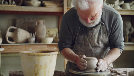 senior potter shaping clay on pottery wheel in studio