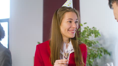 Glückliche-Blonde-Frau-Mit-Partyhut,-Die-Champagner-Trinkt-Und-Mit-Einem-Kollegen-Auf-Der-Büroparty-Spricht