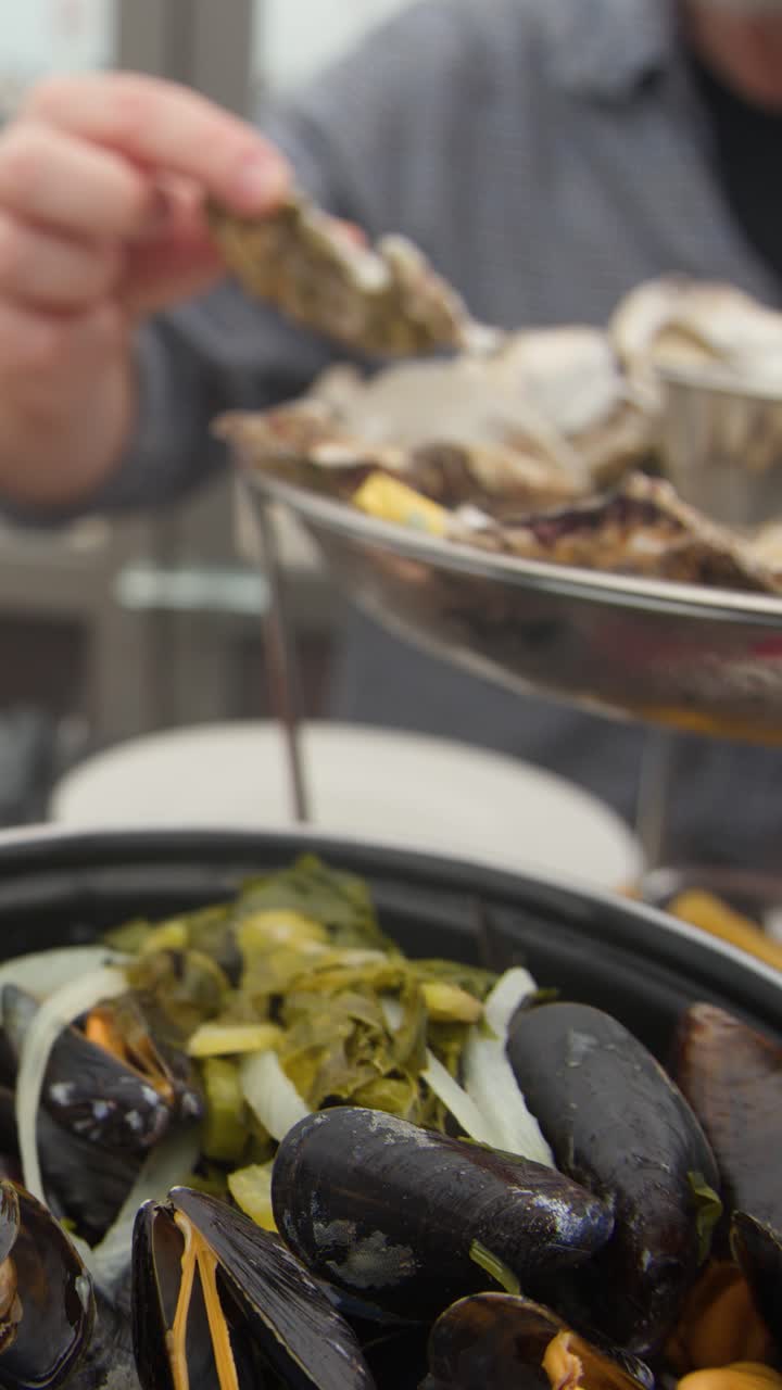Middle-aged man eating oysters and mussels at outdoor coastal restaurant, natural daylight, shallow focus